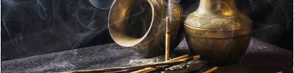 stick of incense burning in front of brass vessels on an old wooden table