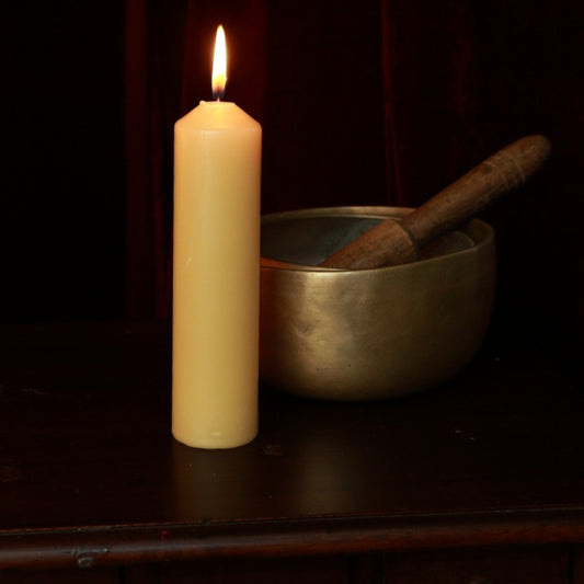 Beeswax pillar candle next to brass singing bowls