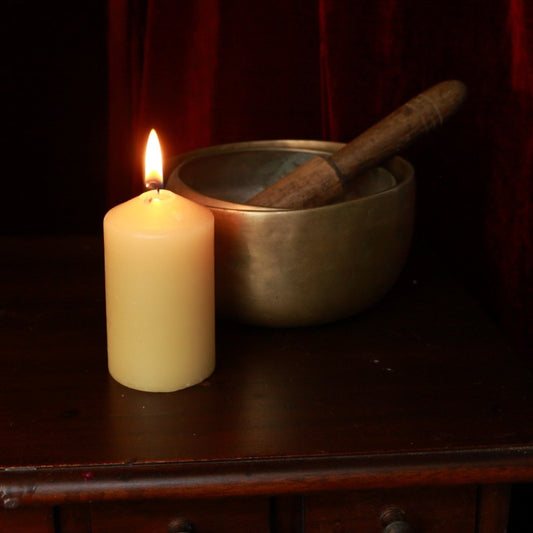 Beeswax pillar candle next to brass singing bowls