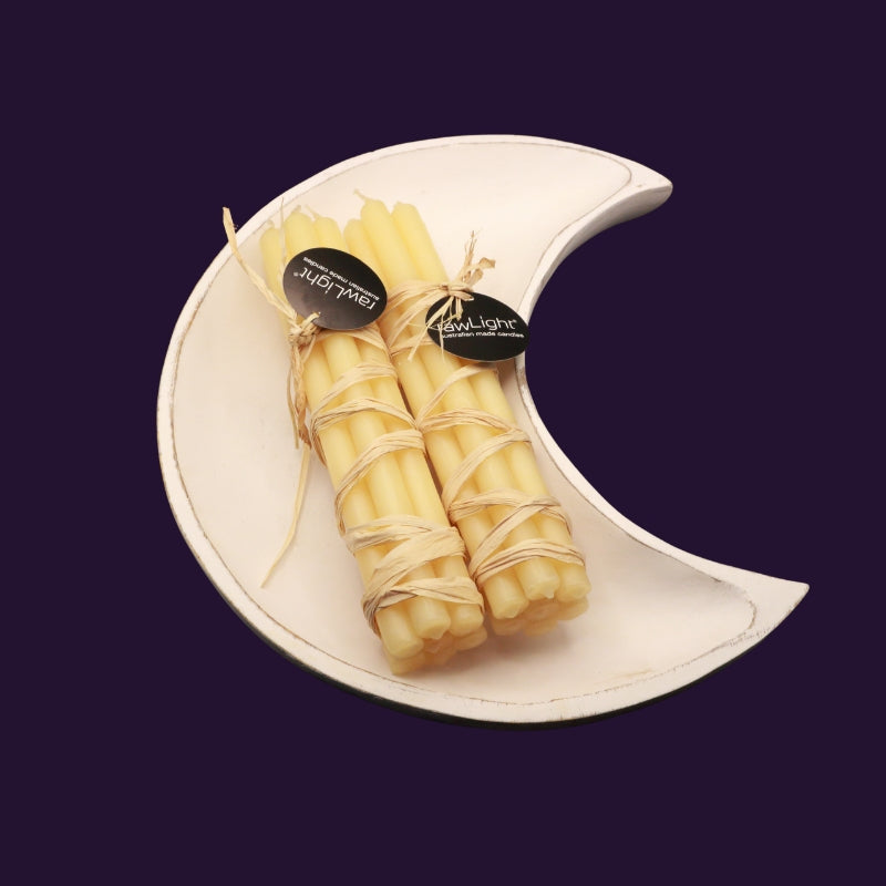 bundles of beeswax prayer candles sitting on a whitewash crescent moon shaped wooden bowl on a purple background