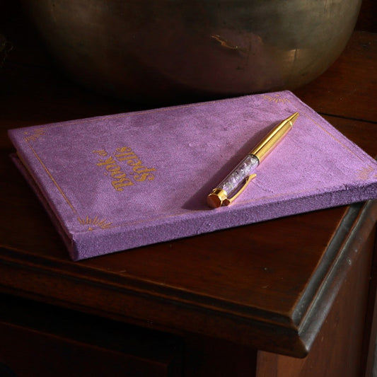 Purple Book of spells journal with amethyst chip gold pen on wooden table