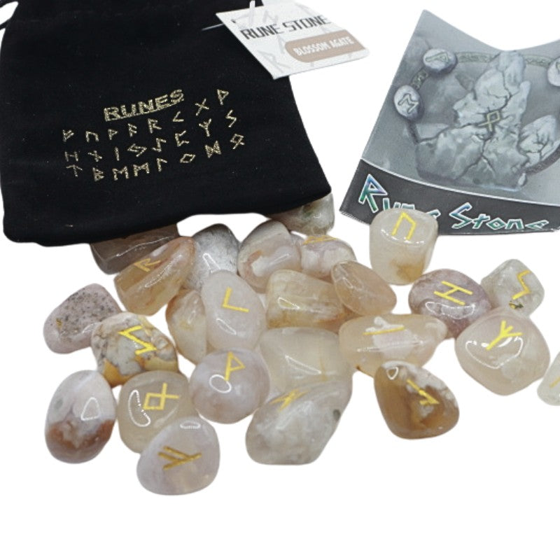 Black velvet bag with gold runic alphabet on front next to a set of blossom agate runes and a rune guide booklet