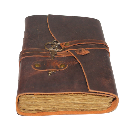 Antique style brown leather journal with a skeleton key on leather band that wraps around to close the cover. Inside contains plain "antiqued" pages