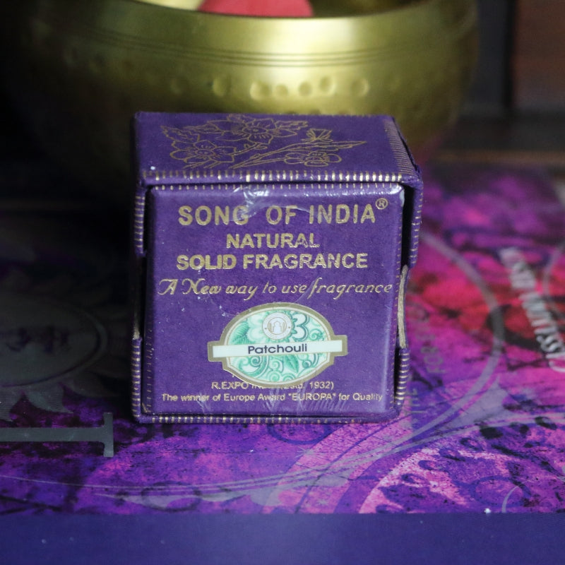 purple and gold box , sitting on a purple and pink book of spells in front of a brass singing bowl with wooden striker.