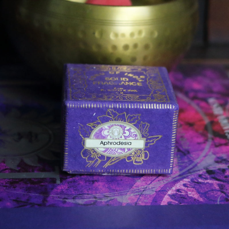 purple and gold box , sitting on a purple and pink book of spells in front of a brass singing bowl with wooden striker.