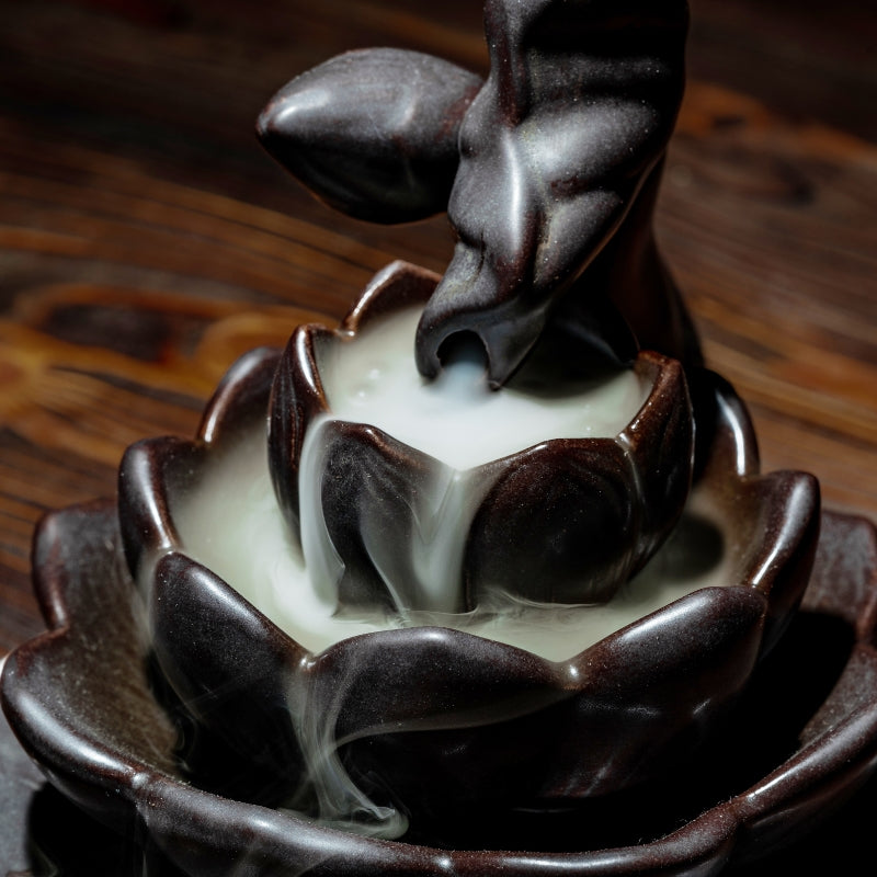 ceramic backflow lotus incense burner with smoke billowing out of the stem, on a wooden table