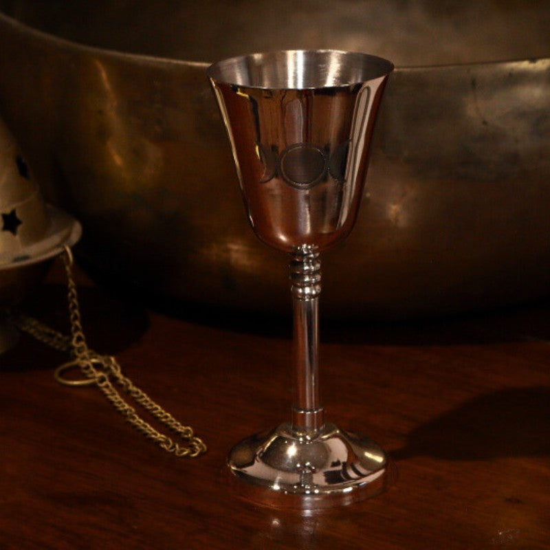Silver goblet with engraved triple moon design on a wooden surface