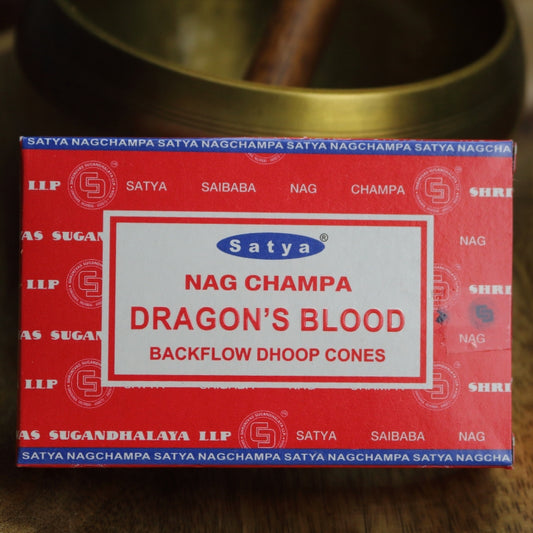 red box of satya backflow incense cones sitting on a wooden table in front of a brass singing bowl with wooden striker