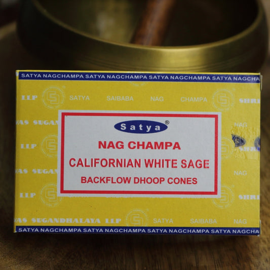 yellow box of satya backflow incense cones sitting on a wooden table in front of a brass singing bowl with wooden striker