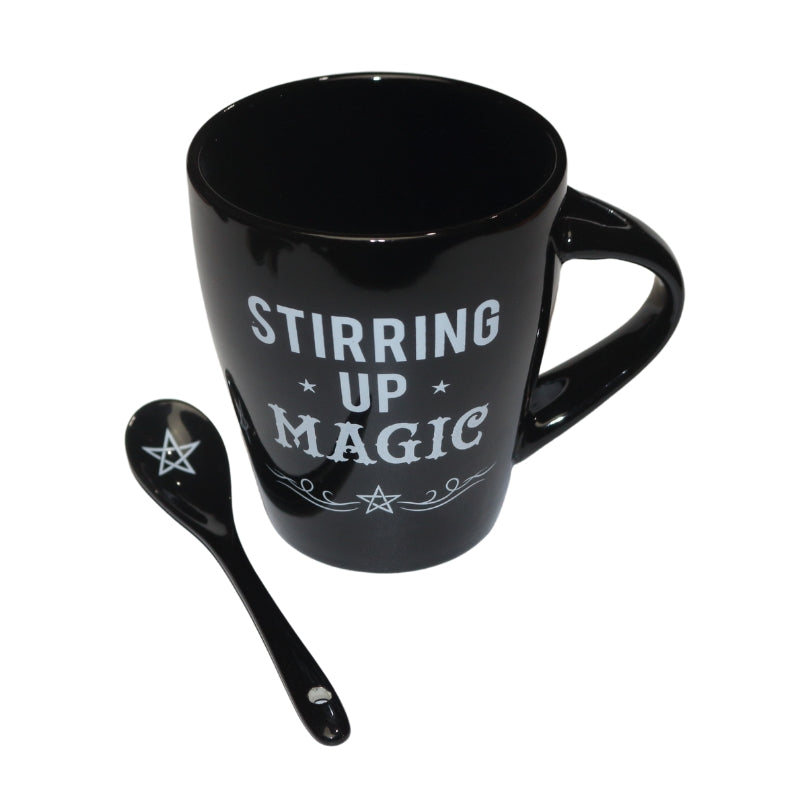 black mug decorated with the words "stirring up magic " written in white, and black spoon decorated with a white pentacle.