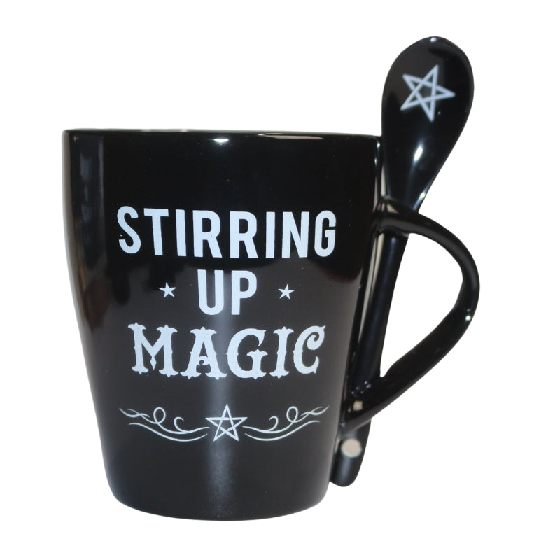 black mug decorated with the words "stirring up magic " written in white, and black spoon decorated with a white pentacle.