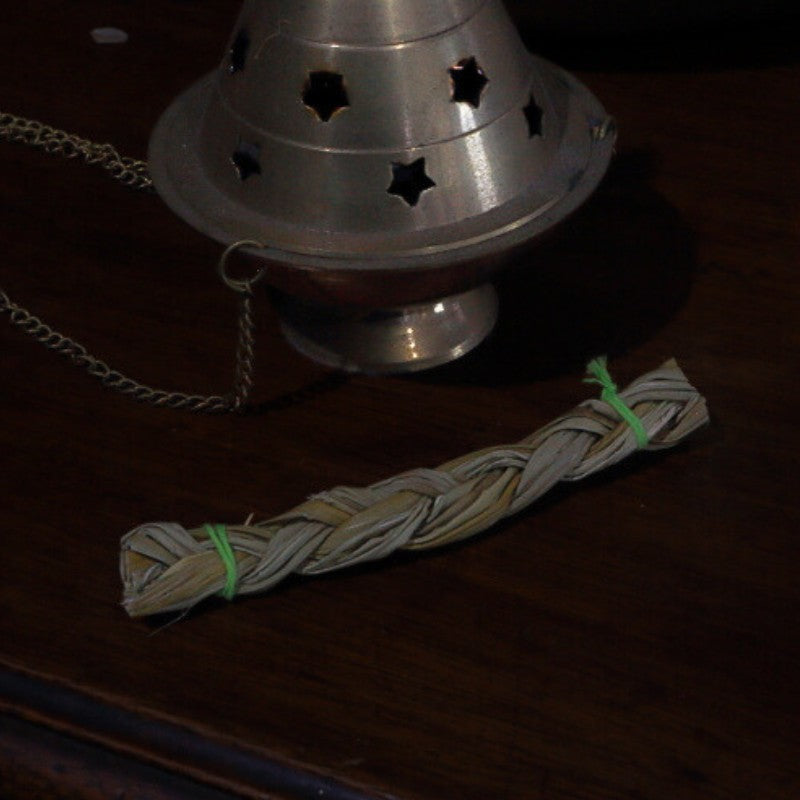 brass incense burner with a braid of sweetgrass on a dark surface