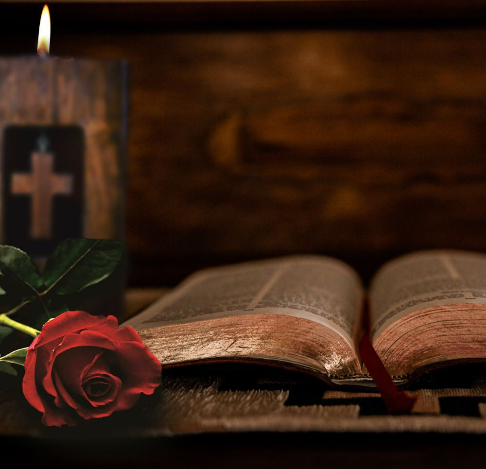 cross wooden tealight candle holder solid hardwood with white tea light in top behind a red rose and an old book, in front of a wooden background
