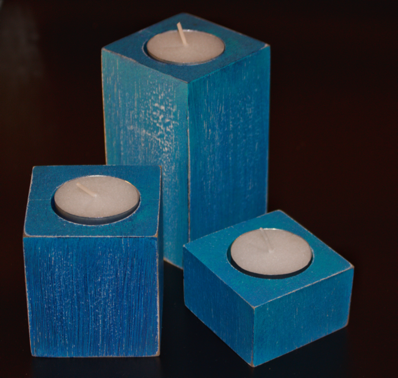 3 blue distressed square candles holding white tea lights, on a black background