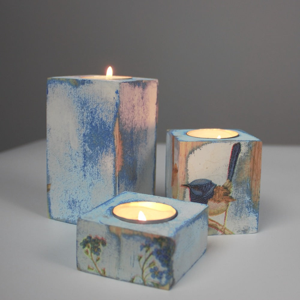 blue and white distressed set of 3 candle holders with lit tea light candles, decorated with fairy wrens and blue flowers