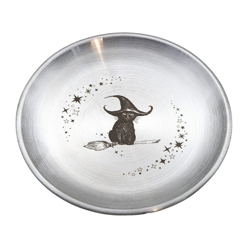 A round brushed silver metal bowl featuring a black illustration of a witch sitting on a broomstick, surrounded by stars and dots, on a white background.