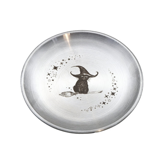 A round brushed silver metal bowl featuring a black illustration of a witch sitting on a broomstick, surrounded by small stars, on a plain white background.