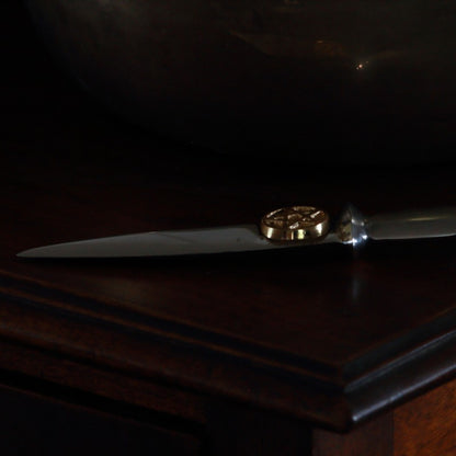 aluminium athame/ dagger with a gold pentacle beneath the hilt laying on a wooden table