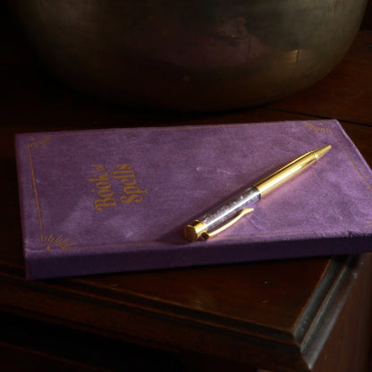 Purple Book of spells journal with amethyst chip gold pen on wooden table