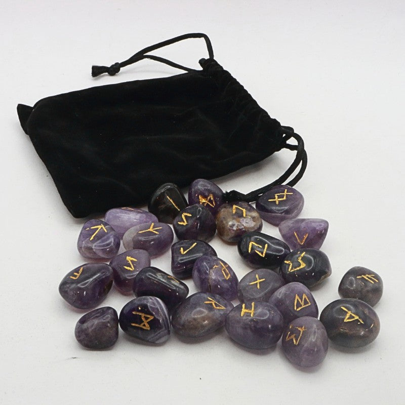 Set of purple stones with gold runes next to a black drawstring bag on a white background