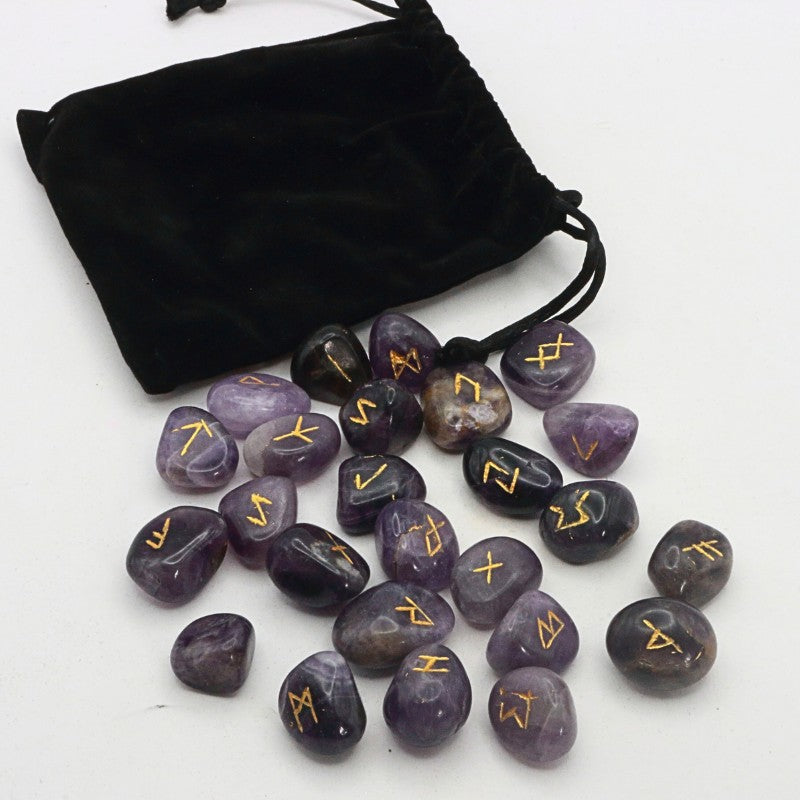 Purple stones with gold runes next to a black drawstring bag on a white background