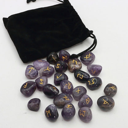 Purple stones with gold runes next to a black drawstring bag on a white background