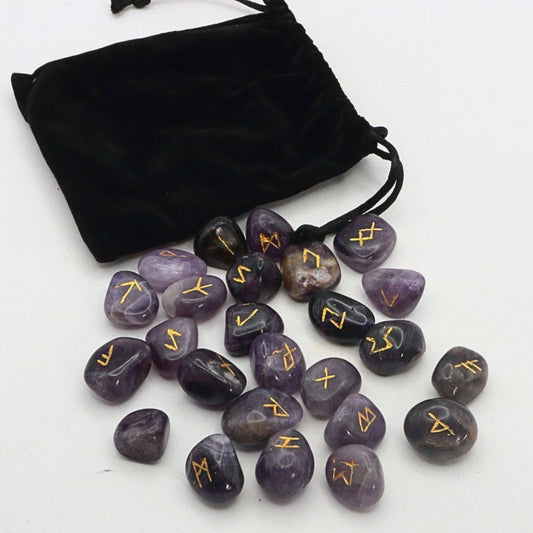 Purple stones with gold runes next to a black drawstring bag on a white background