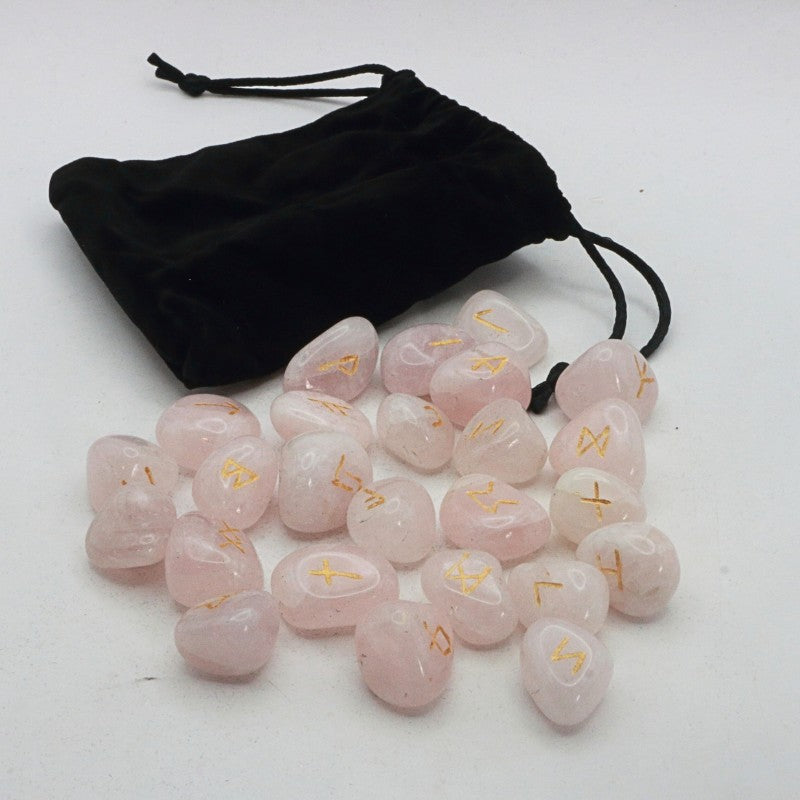 Set of pink crystal runes with gold symbols on a white surface, accompanied by a black drawstring bag.