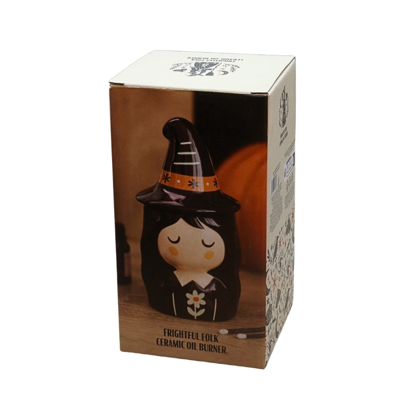 A ceramic oil burner figurine of a witch character in a black hat with orange stripes, shown inside its retail packaging box against a white background.