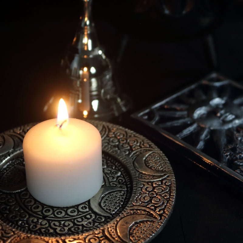 silver triple moon incense holder underneath a lit candle 