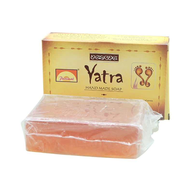Peach-coloured Parimal Yatra handmade soap bar in clear wrapping, displayed in front of its gold box.