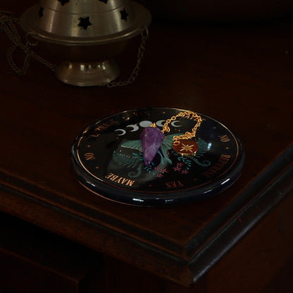 Decorative plate with celestial design  and amethyst pendulum 
on a dark surface