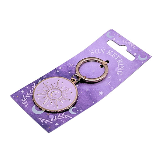 A circular sun keyring charm with a gold-tone metal frame and a pale lavender center featuring a sun design, attached to a purple card backing labeled 'SUN KEYRING'.