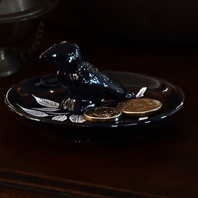 Black ceramic dish with a bird design on a dark surface