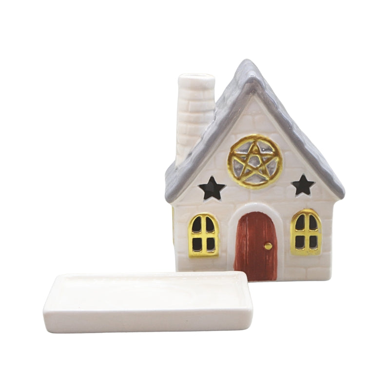 A small decorative house-shaped object with a gray roof, white body, red door, gold window trim, black stars, and a pentagram emblem on the front, shown alongside a rectangular white tray on a plain white background.