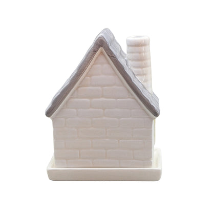 A small ceramic house-shaped container or candle holder with a textured off-white brick pattern, a gray roof, and a matching off-white chimney and base, shown on a plain white background.