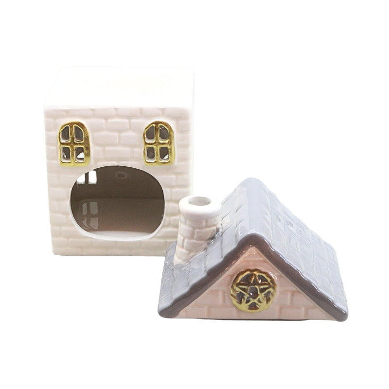 A small decorative house-shaped ceramic object shown from two angles on a plain white background. The front view shows a cream brick-textured body with two gold-trimmed arched windows and a round opening; the side view shows a gray textured roof with a small white chimney and a gold circular emblem.