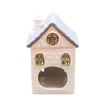 A small decorative house-shaped ceramic object with a pale cream brick-textured body, gray roof, gold window and star details, and a dark opening at the bottom, shown on a plain white background.