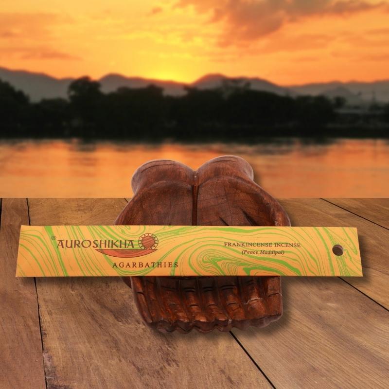 pk of auroshikha incense sitting on a carved wooden hand on a jetty, in front of a golden sunset