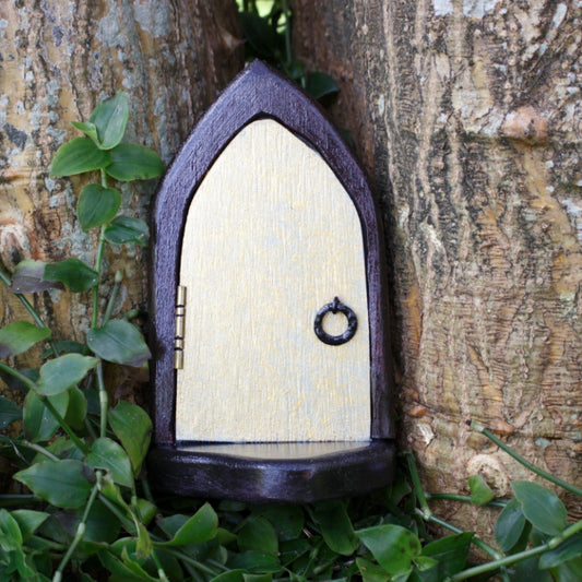 handmade gold fairy door standing in front of a tree